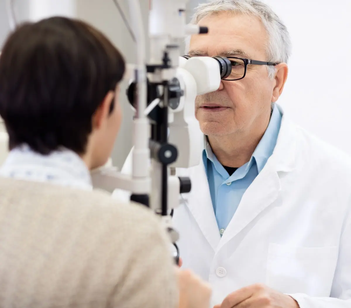 Senior male eye specialist look in ophthalmoscope and perform eye review